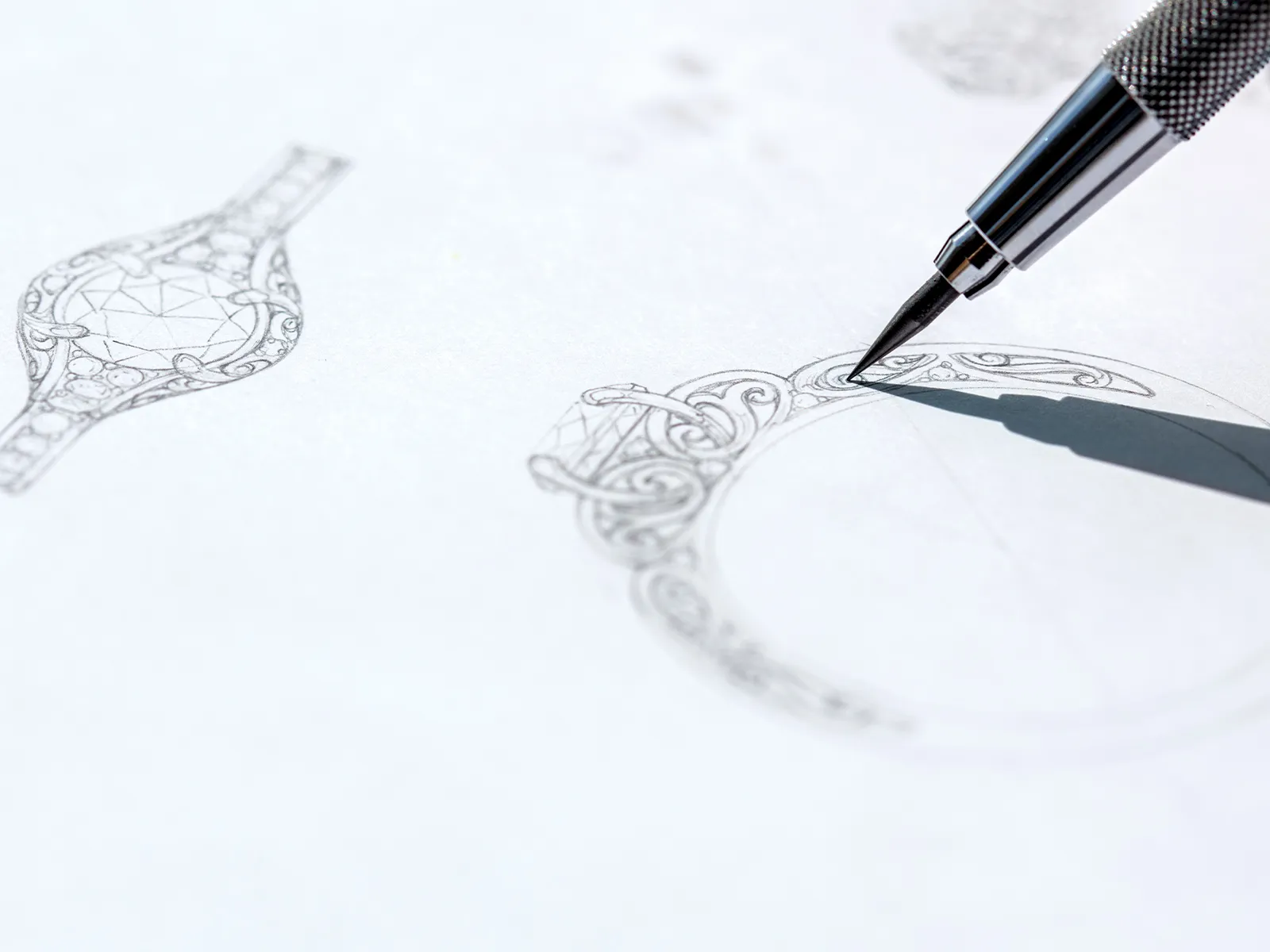 A pen sketching an intricate ring design on paper.