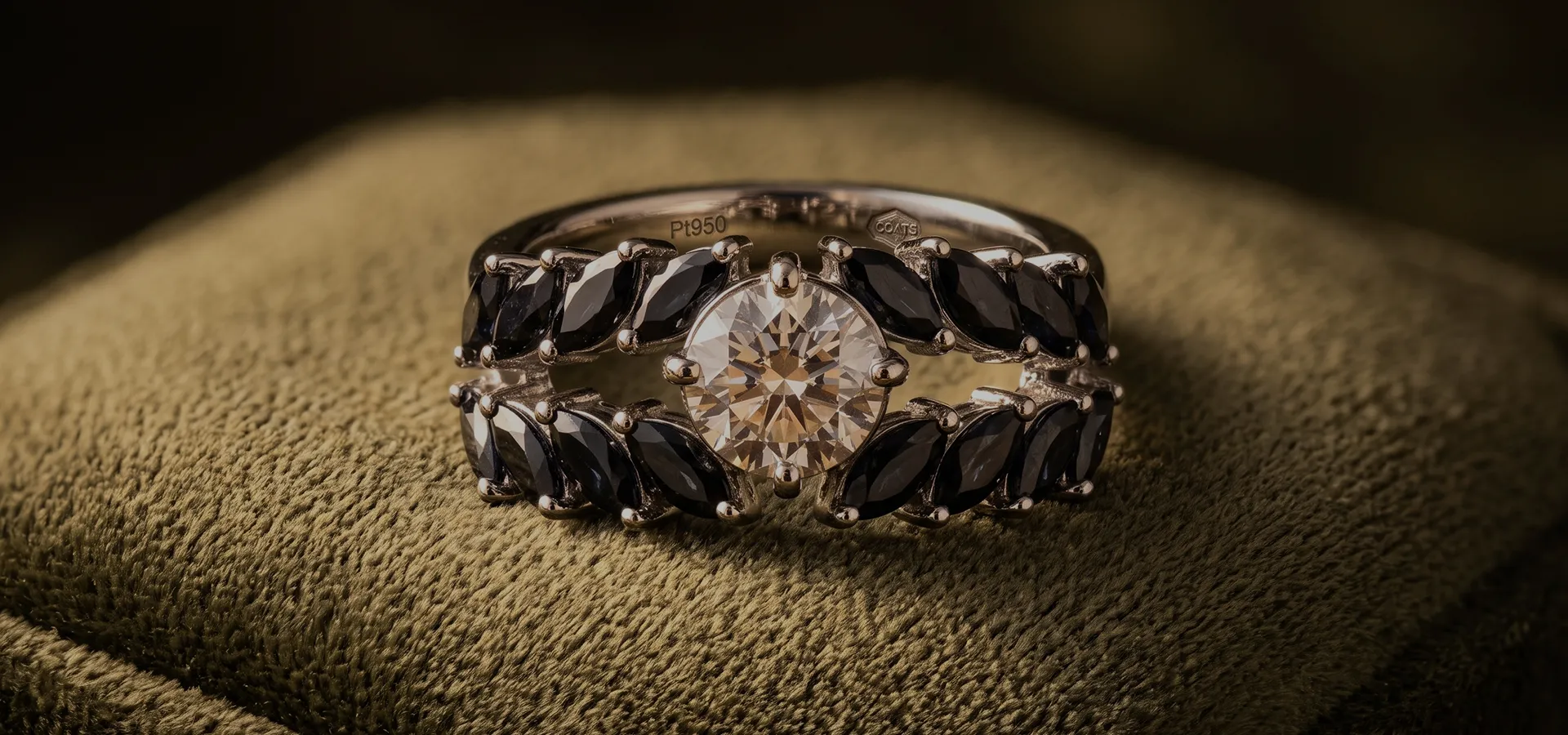 A platinum ring with a central diamond and marquise black stones on a textured surface.