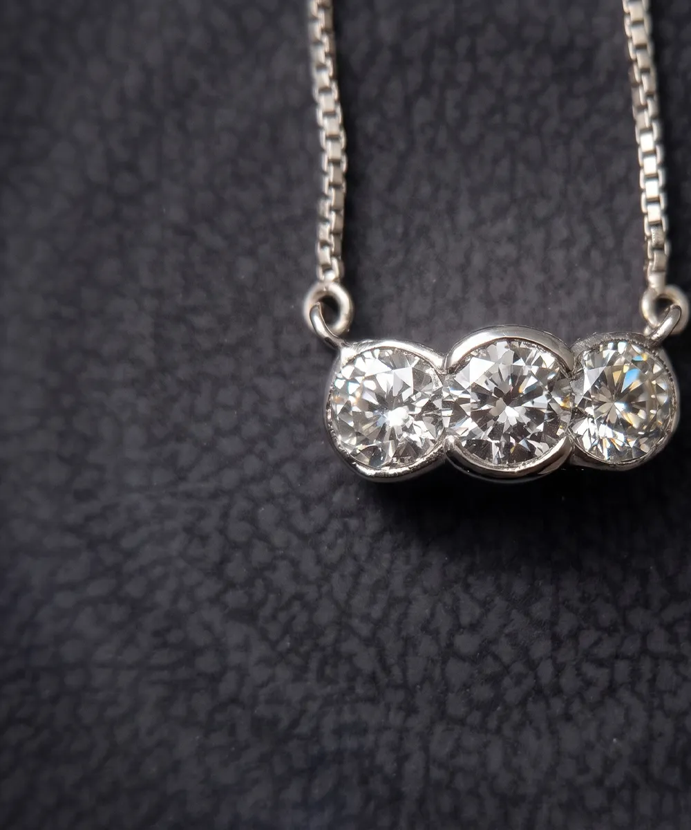 A necklace with three round diamonds set in a row on a textured dark background.