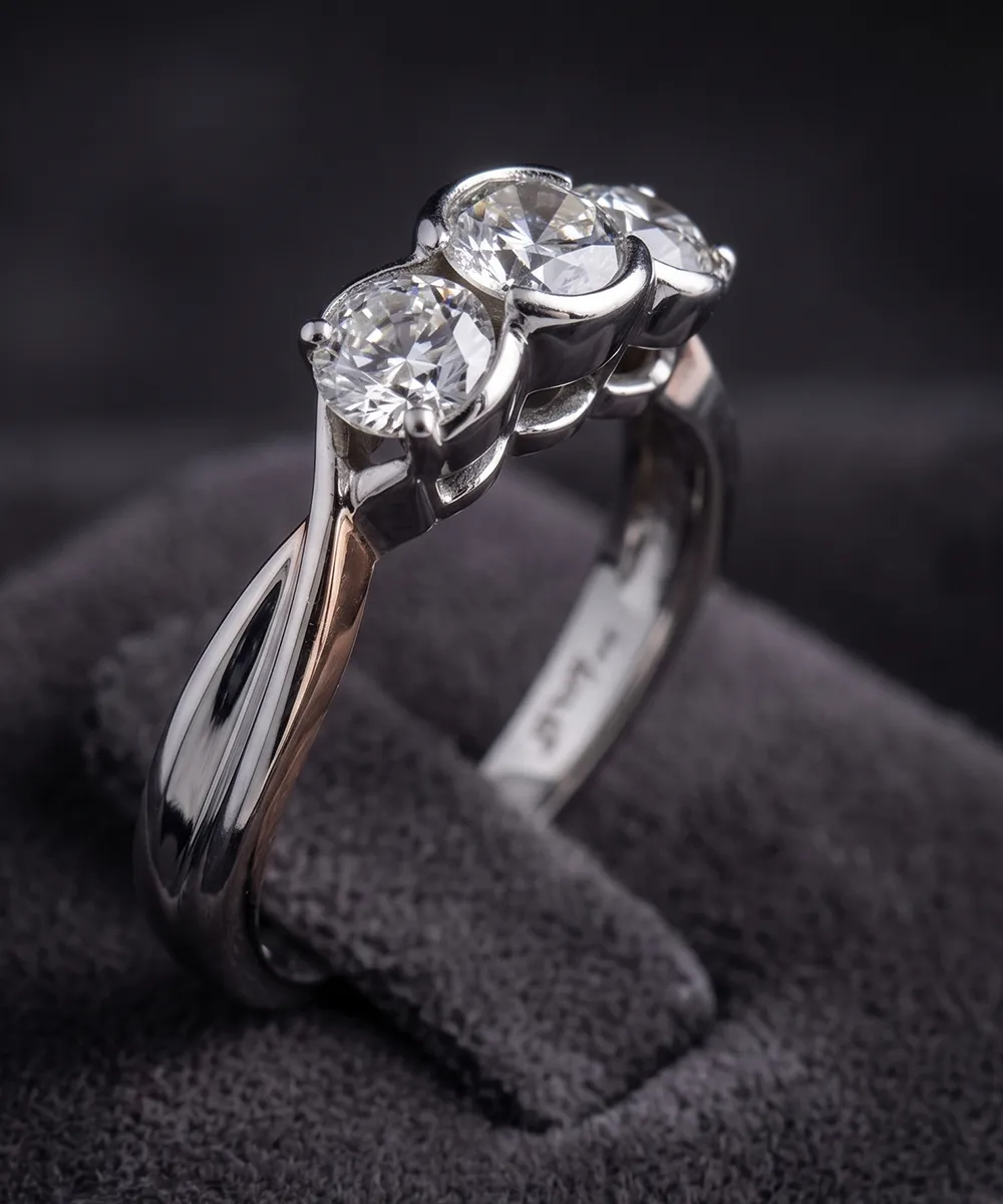 A silver ring with three round diamonds set on a dark fabric background.