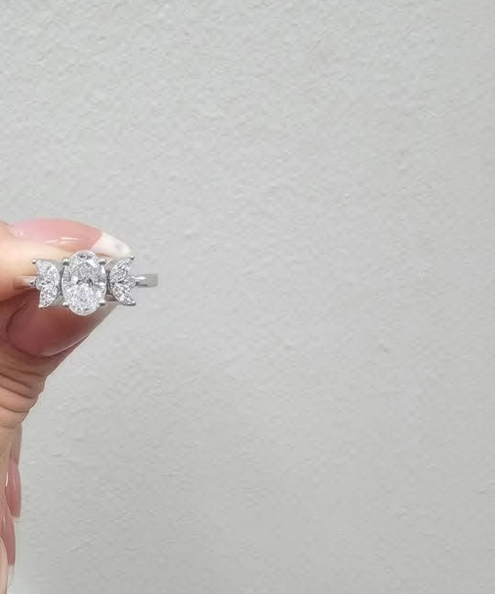 A hand holding a three-stone diamond ring against a plain background.