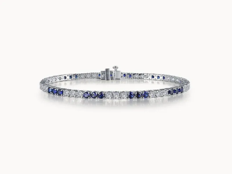A silver bracelet with alternating blue and clear gemstones on a white background.