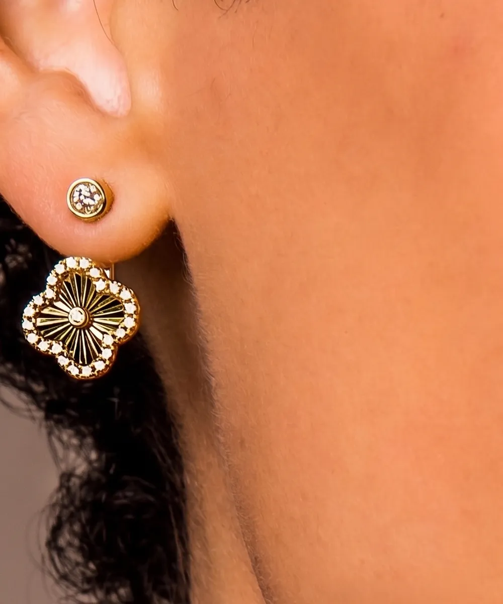 Close-up of an ear wearing a small diamond stud and a decorative gold earring with a floral design.