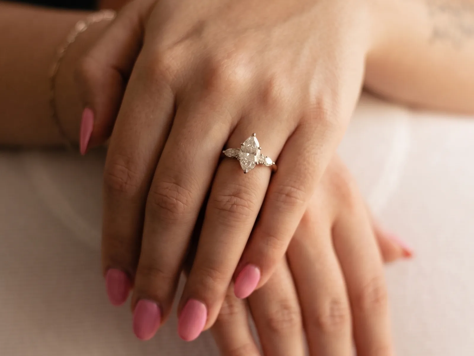 A hand with pink nails wearing a pear-shaped diamond ring.