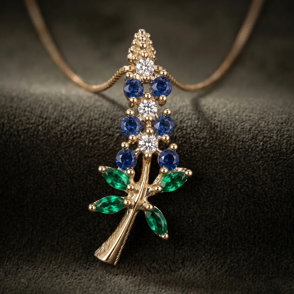 Gold pendant with blue, green, and clear gemstones arranged in a floral design on a chain.