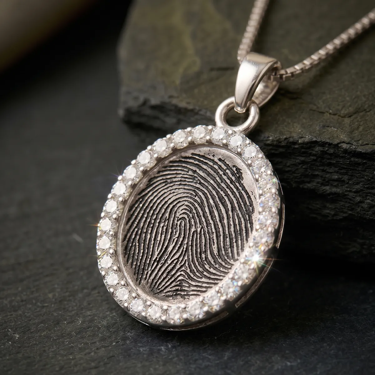 A silver pendant with a fingerprint design, surrounded by sparkling stones, on a chain.