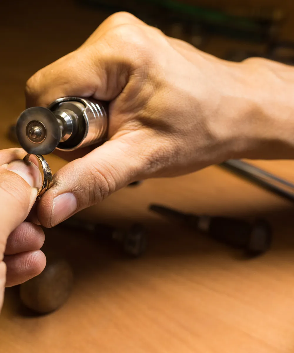 A person polishing a ring with a rotary tool on a wooden workbench.