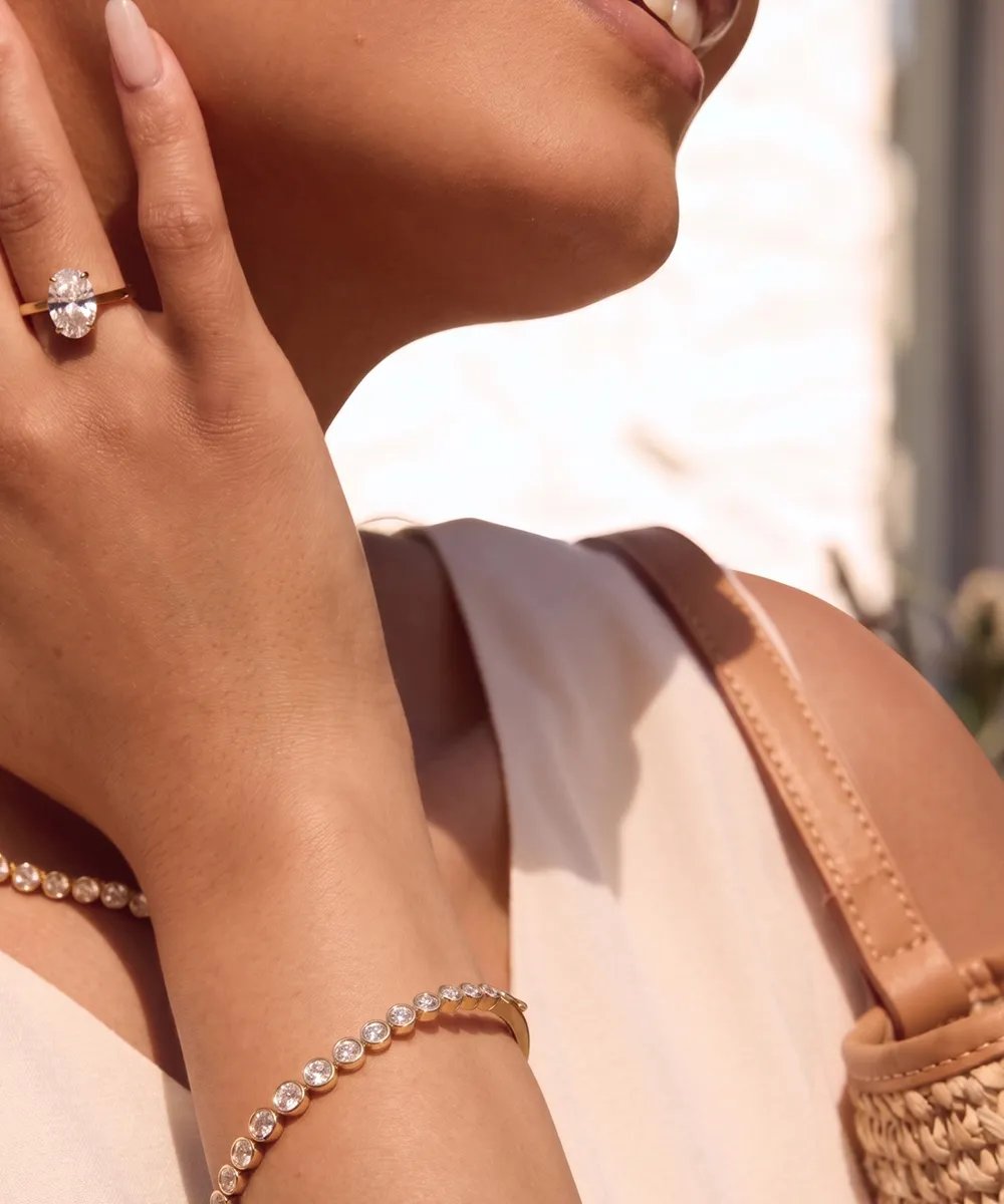 A person wearing a diamond ring and bracelet, holding their hand to their face.