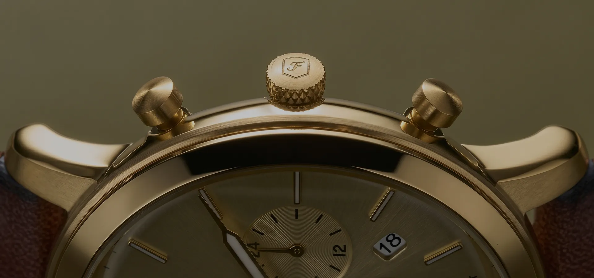 Close-up of a gold watch with a textured crown and pushers, displaying part of the dial and date window.