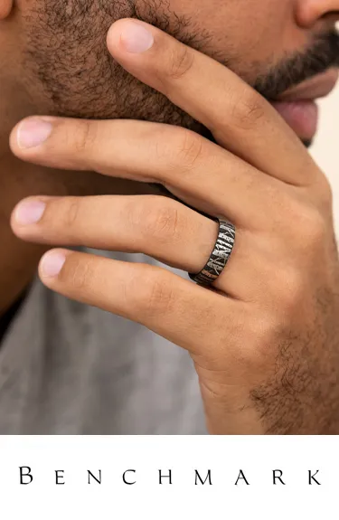 Man's hand showcasing a textured black wedding band by Benchmark. Click to explore more at Dahlkemper's Jewelry Connection.