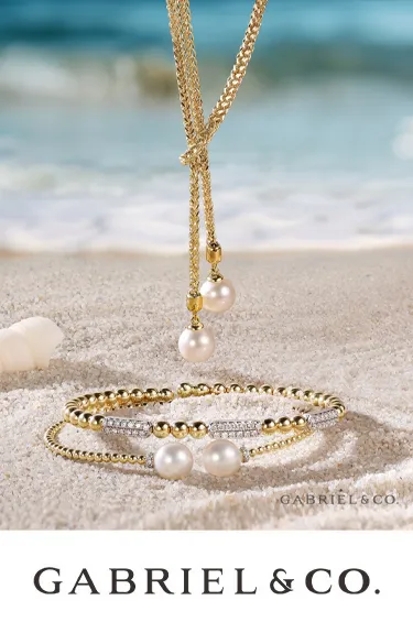 Elegant gold and pearl jewelry by Gabriel & Co. displayed on sandy beach; click to explore more at Dahlkemper's Jewelry Connecti