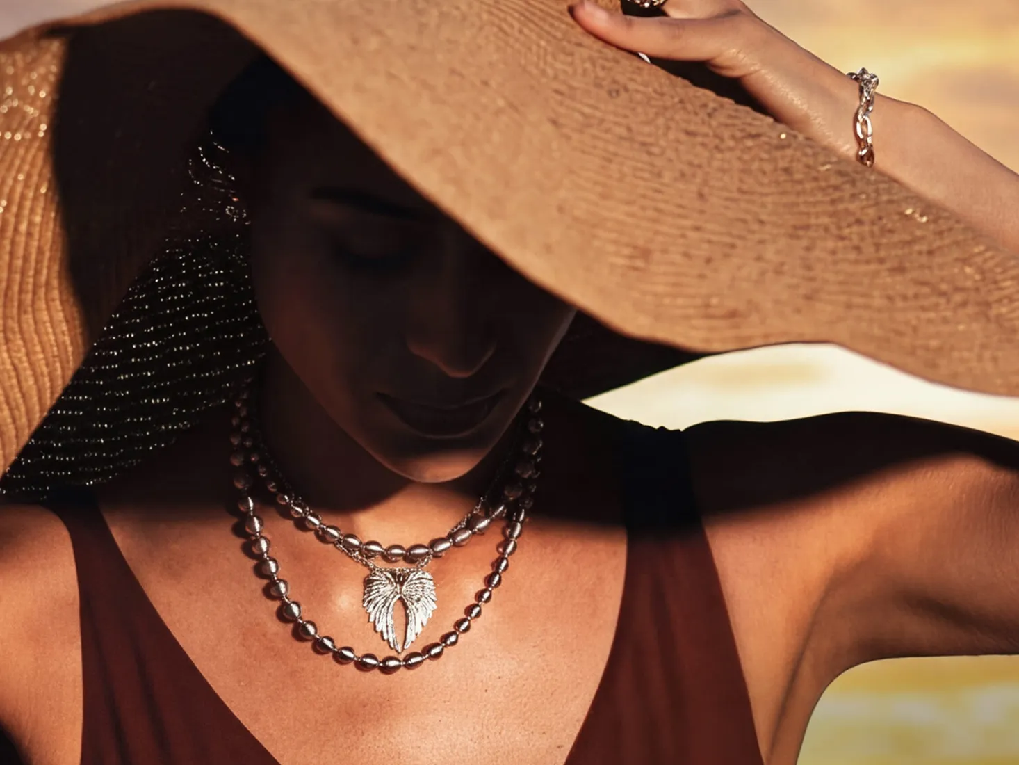 A woman wearing layered necklaces and a large sun hat, partially shadowed.