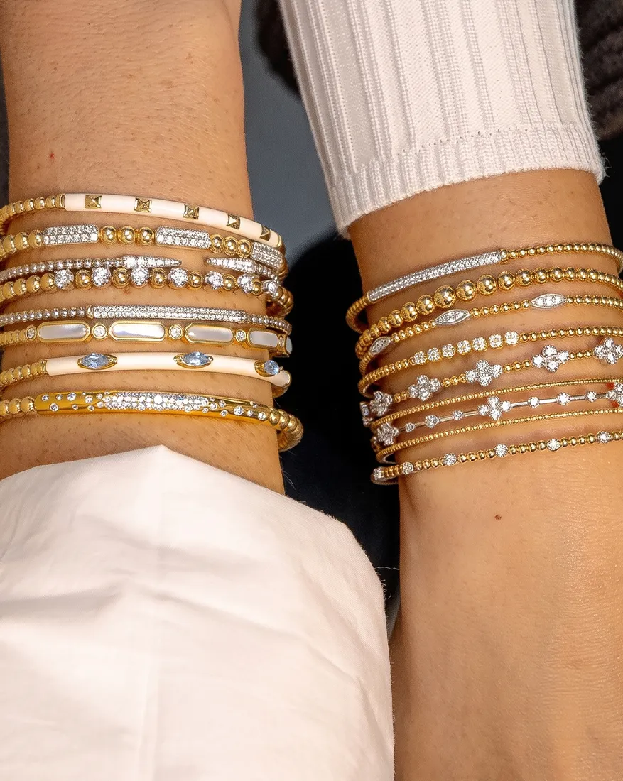 Two wrists adorned with multiple gold and diamond bracelets in various designs.
