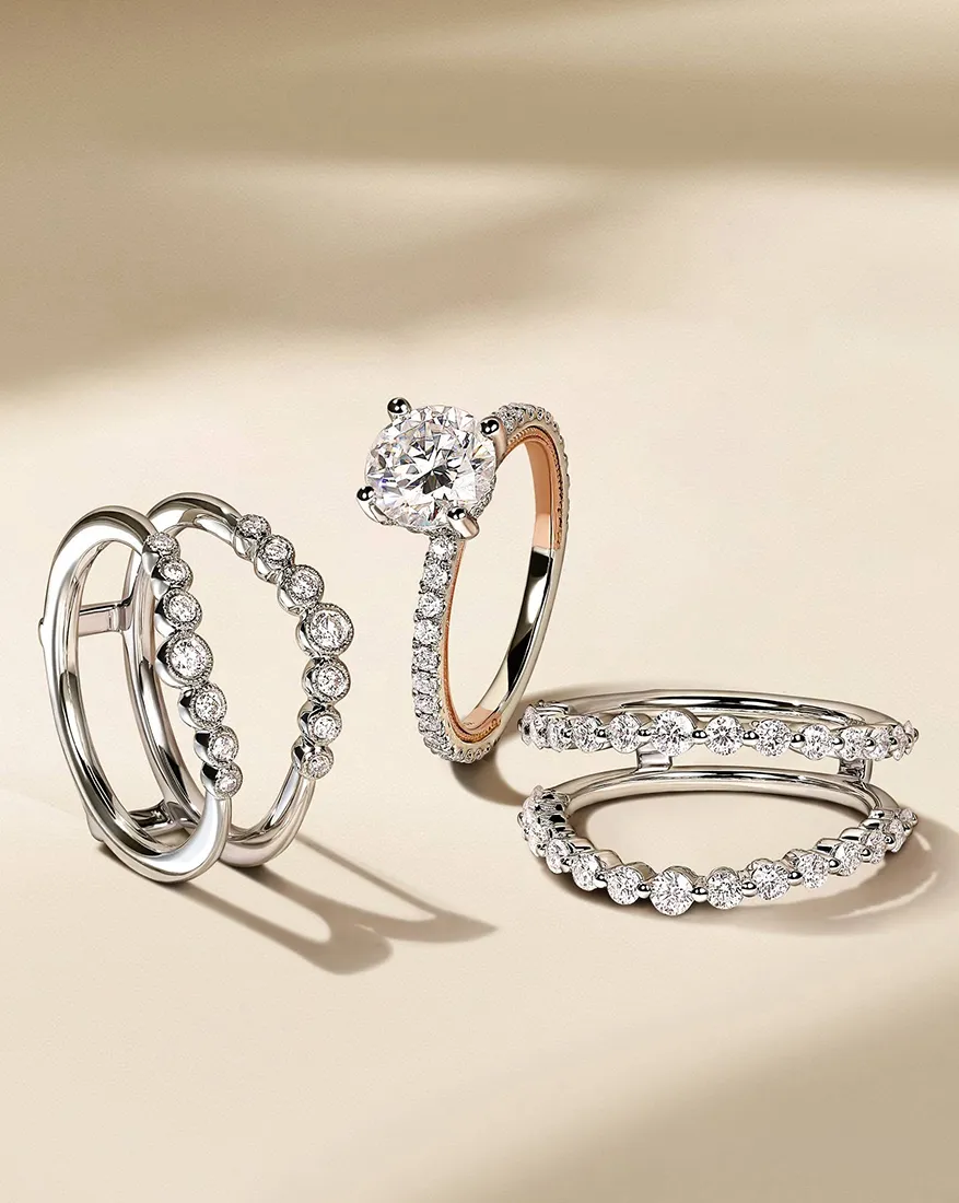 Three elegant diamond rings on a beige surface, featuring a solitaire and two bands with round diamonds.