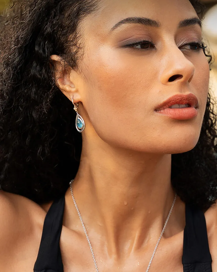 A woman wearing a teardrop-shaped gemstone earring and a necklace, with curly hair and a black top.