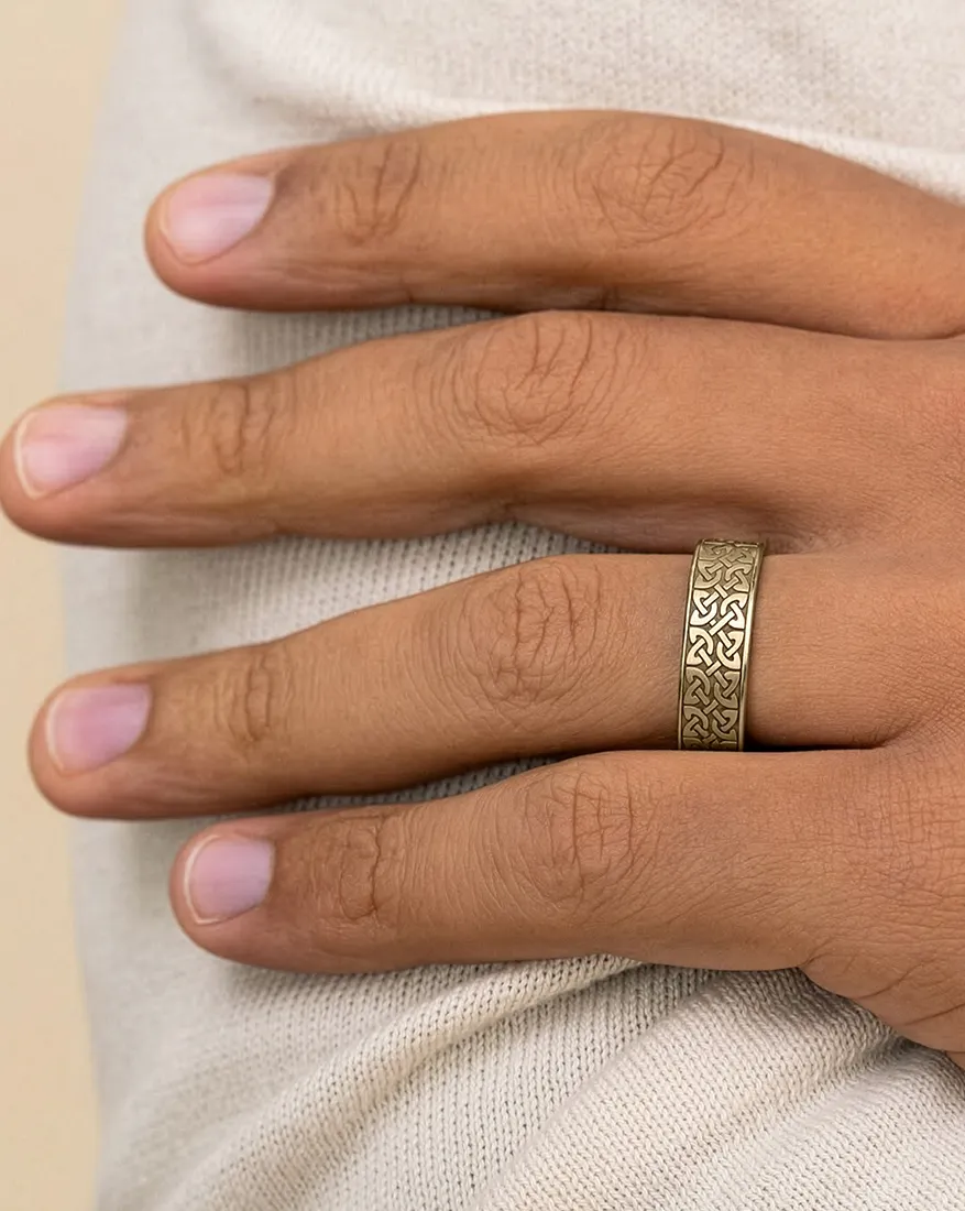 Hand wearing a gold ring with intricate patterns on a light fabric background.