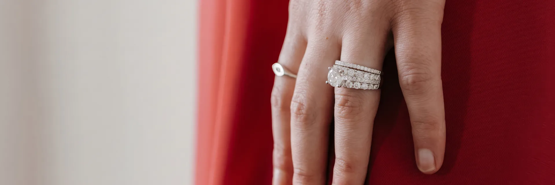 A hand with a diamond bridal ring set against a red background.