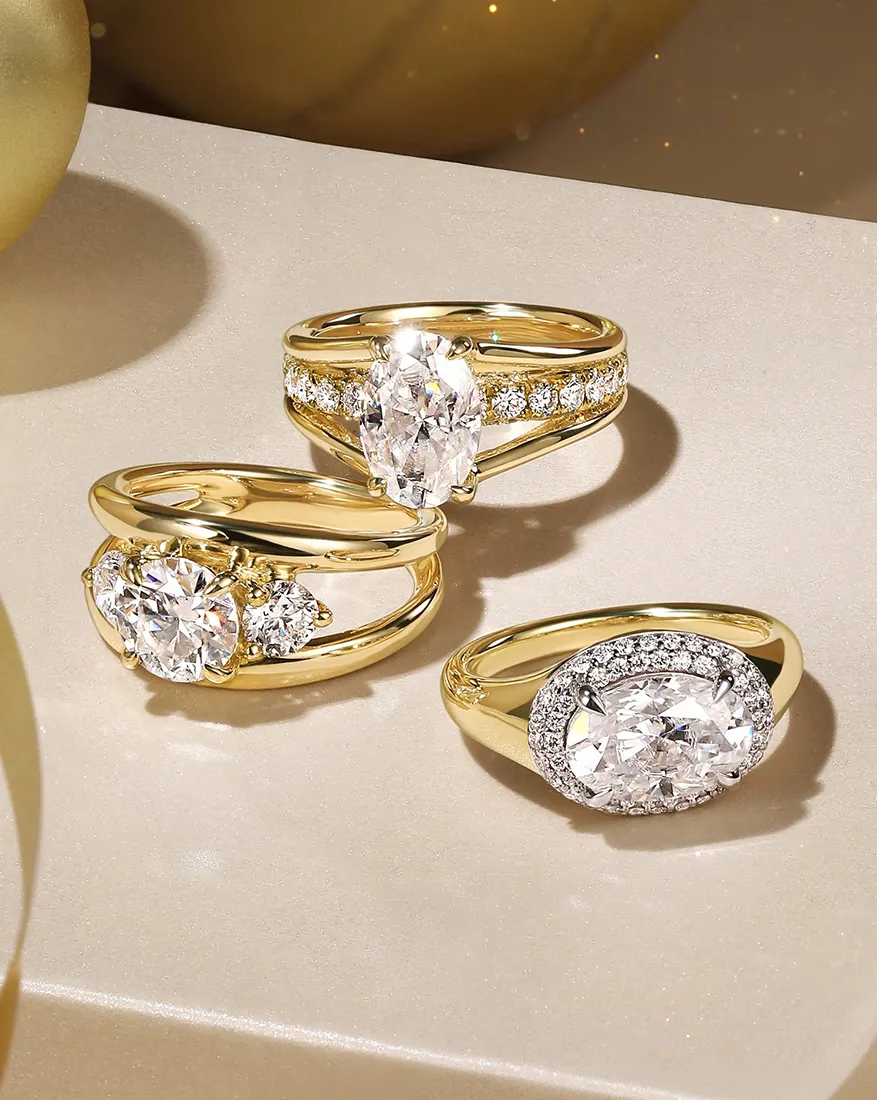 Three gold rings with large diamonds and smaller accent stones on a shimmering surface.