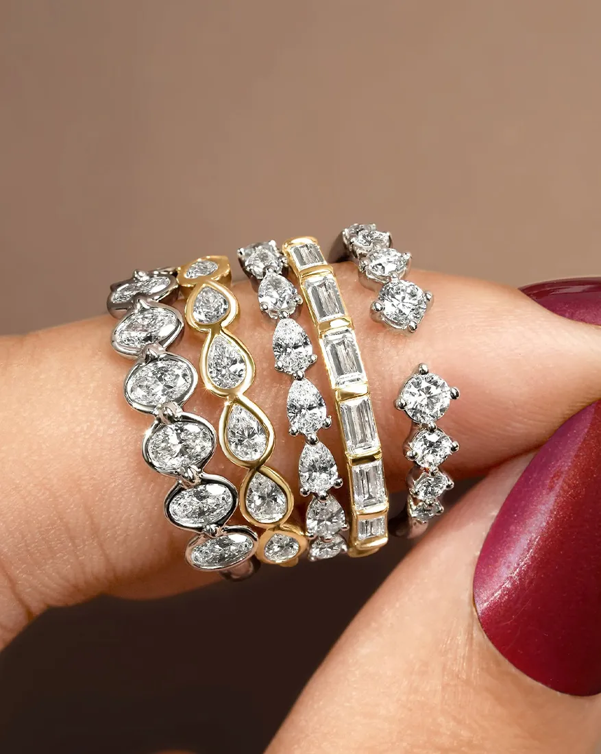 A hand displaying five diamond-studded rings in various designs and metals.