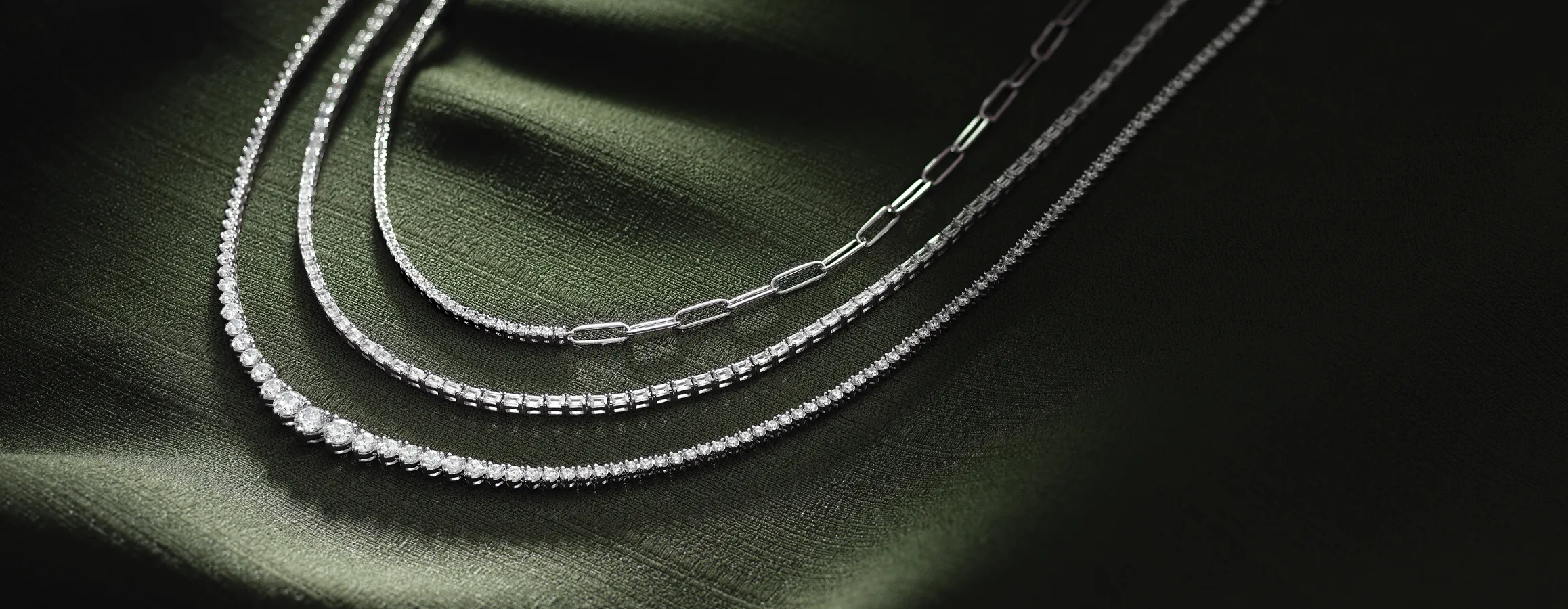Three elegant silver necklaces displayed on a dark green fabric background.