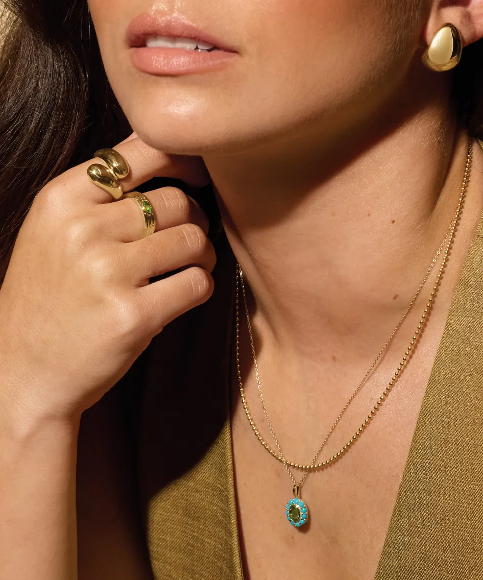 Close-up of a woman wearing gold jewelry, including rings and layered necklaces with a turquoise pendant.