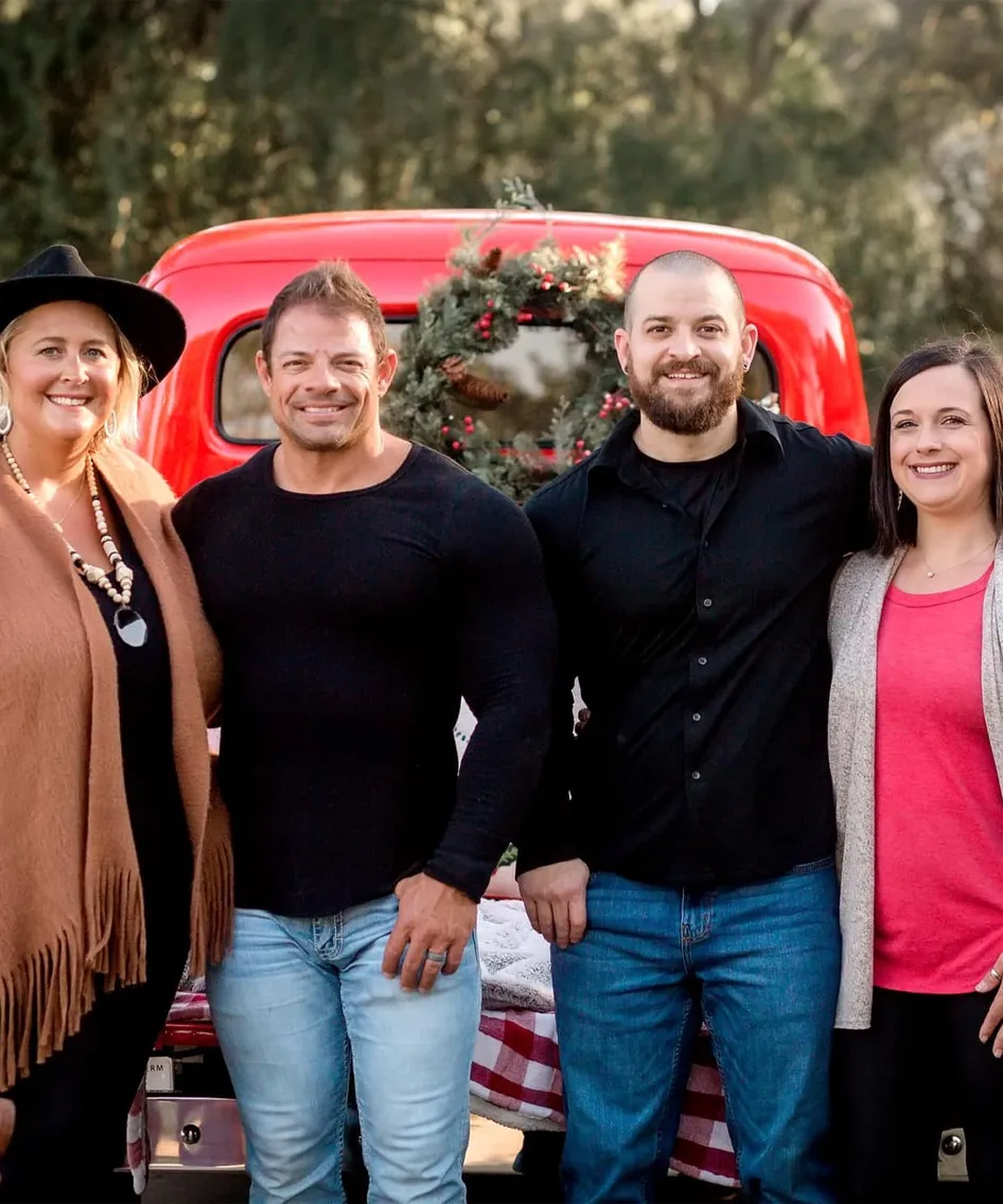 Group of four people smiling in front of a red vintage truck decorated for the holidays.