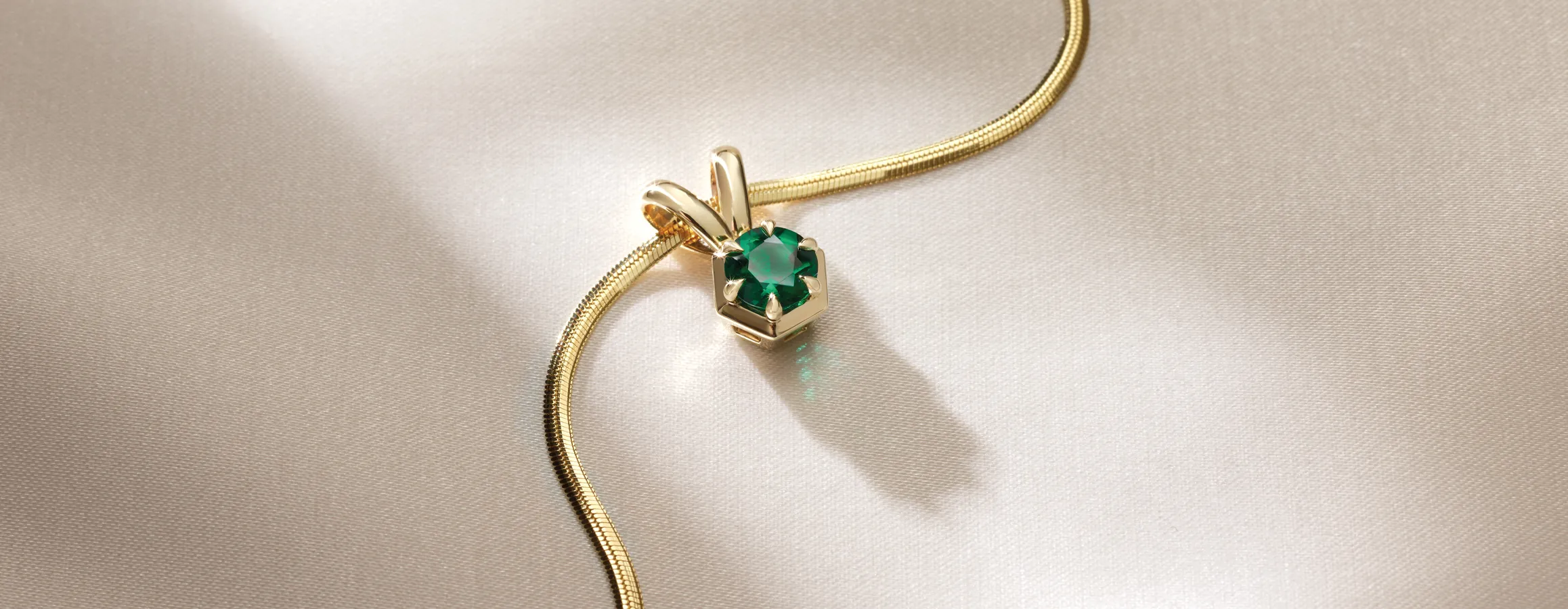 Emerald pendant on a gold chain, displayed on a soft beige fabric background.