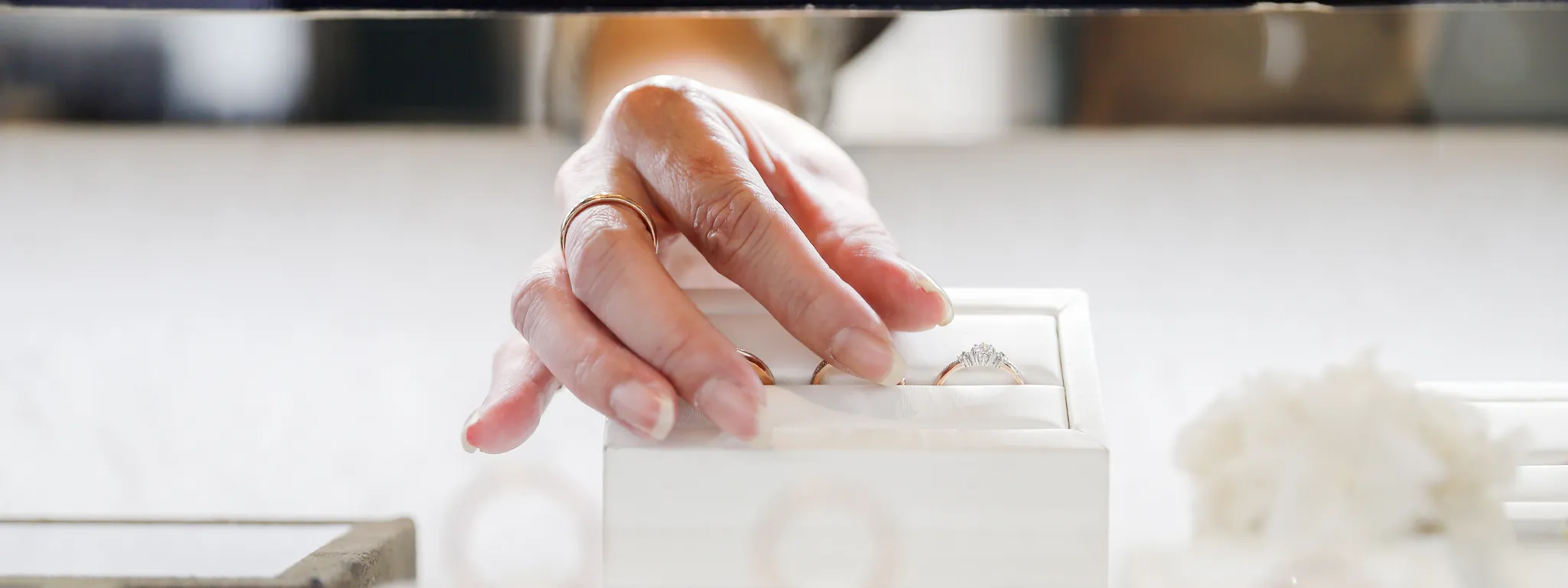 A hand reaching for a diamond engagement ring in a jewelry box.