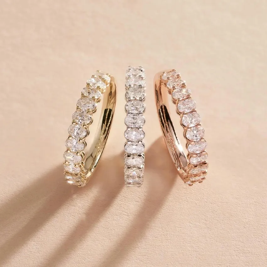 Three elegant women's wedding bands in gold, silver, and rose gold with sparkling stones, displayed on a soft background.