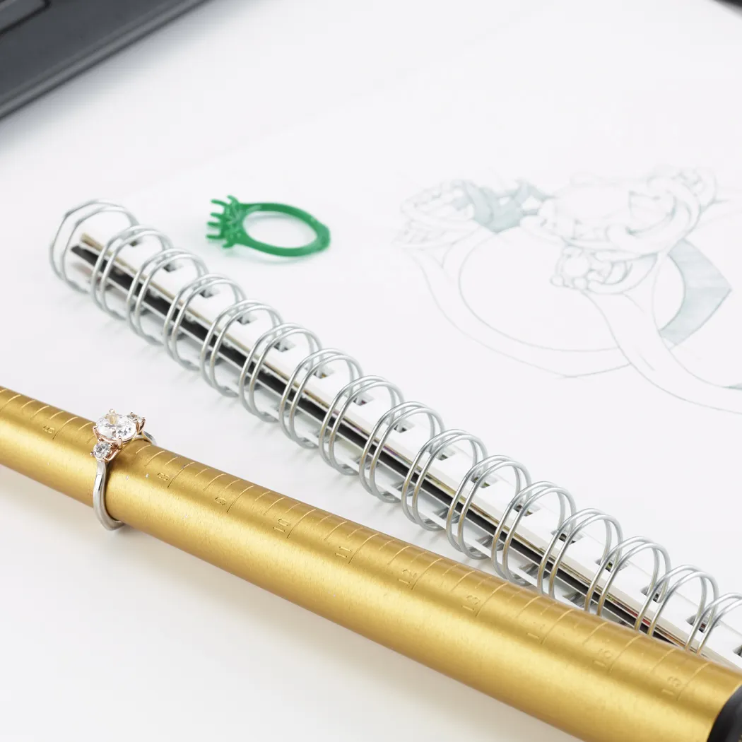Engagement ring on a gold ring sizer with a sketch and notebook.