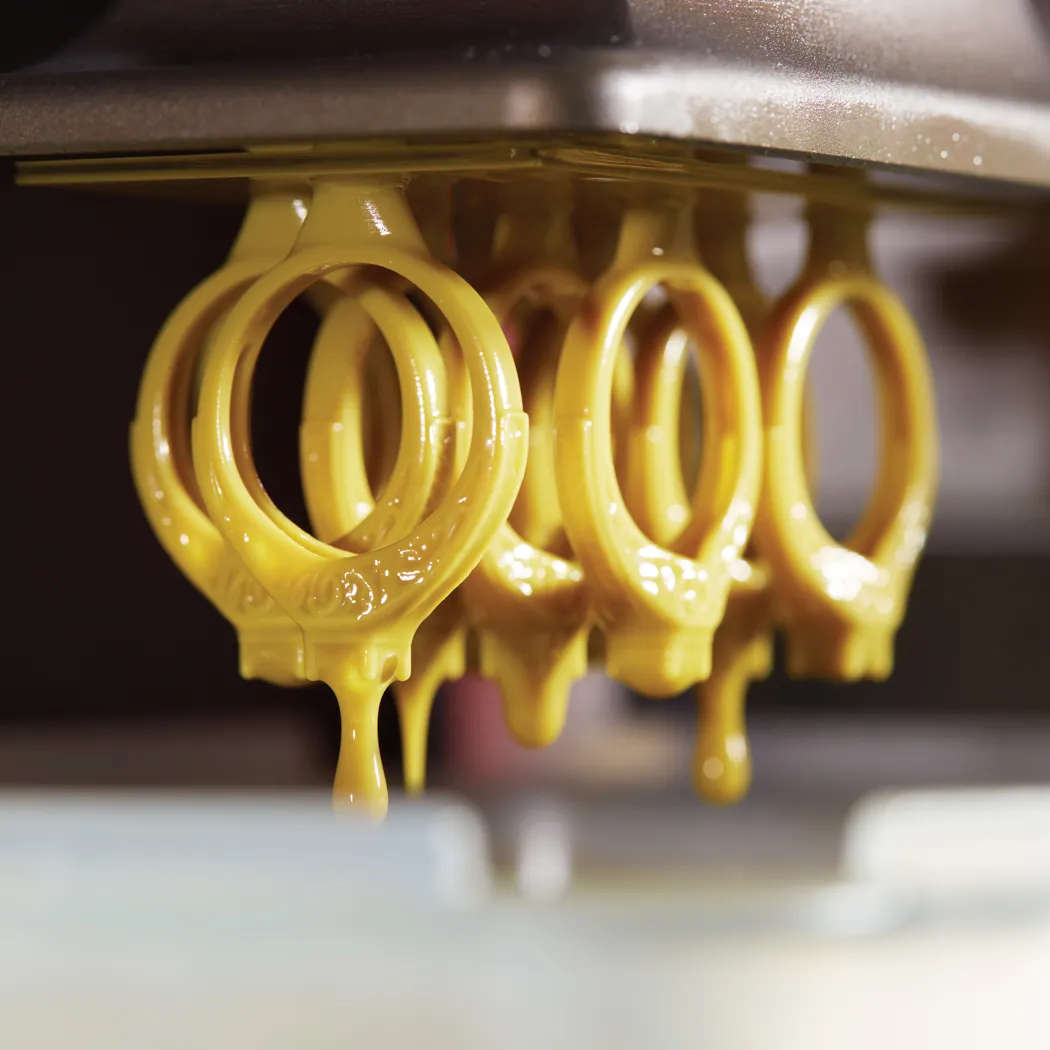 Yellow wax dripping from a jewelry mold, showcasing intricate ring designs.