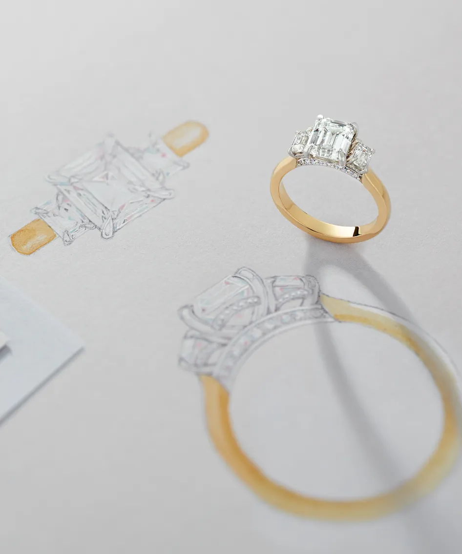 Emerald-cut engagement ring beside its sketch on paper.