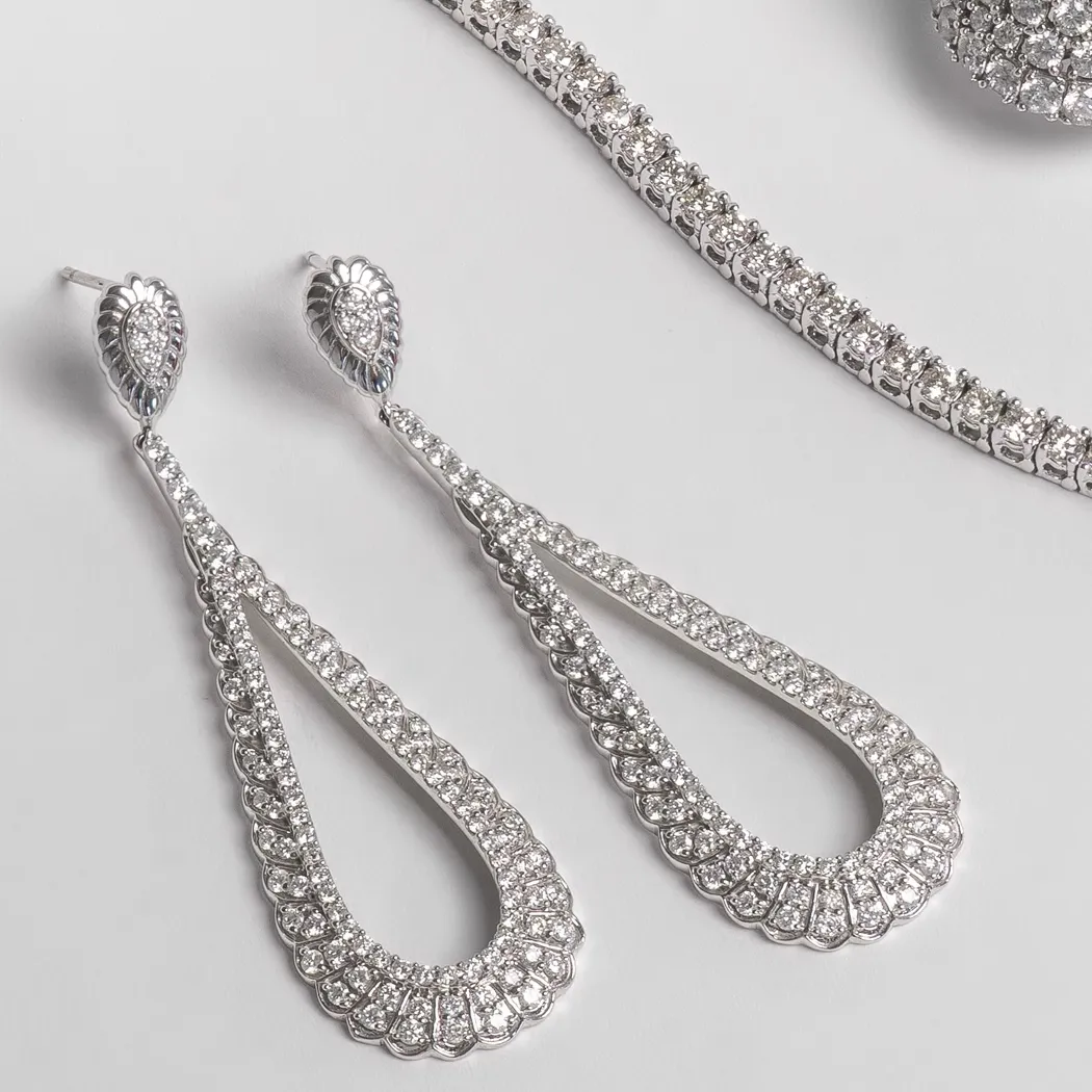 Elegant silver earrings with intricate designs and sparkling diamonds, displayed alongside a matching bracelet.