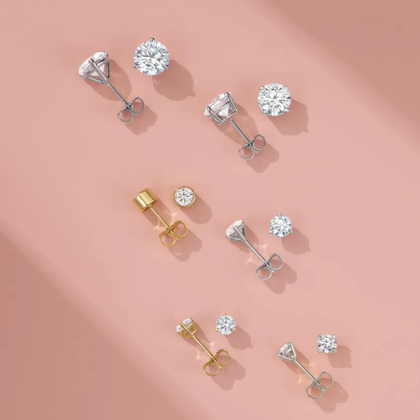Collection of diamond stud earrings in various styles and metals on a soft pink background.
