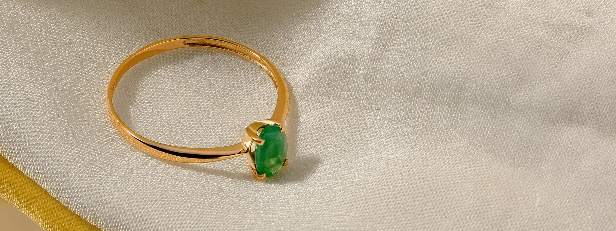 Gold ring with a green stone, elegantly displayed on a soft fabric background.