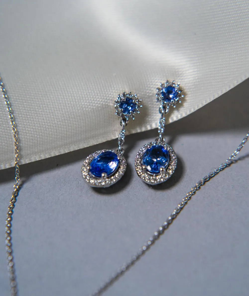Elegant blue gemstone earrings with sparkling accents, displayed on a soft fabric background. 