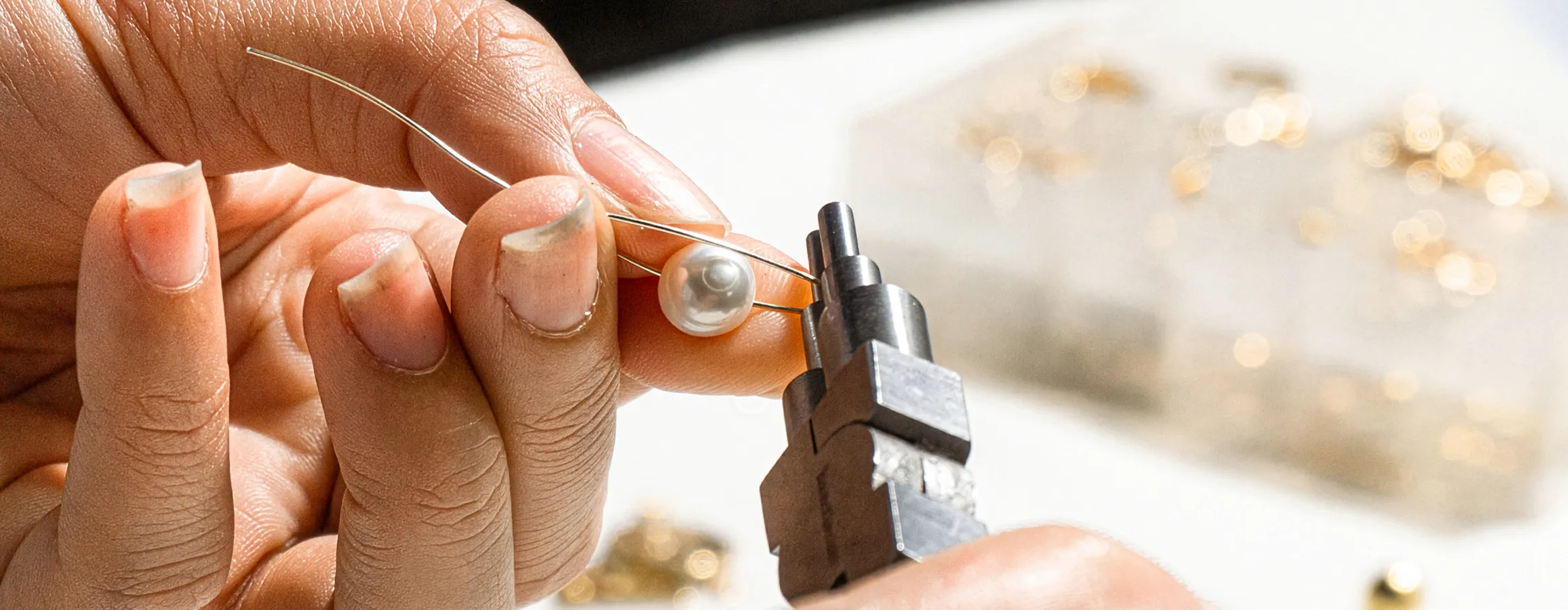 A jeweler carefully threading a pearl onto wire with pliers, showcasing jewelry restoration skills. Click to view our services.