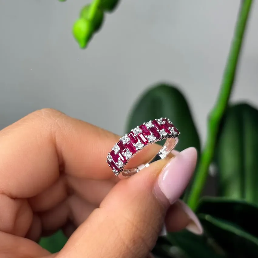 A hand holding a ruby and diamond ring against a blurred green background.