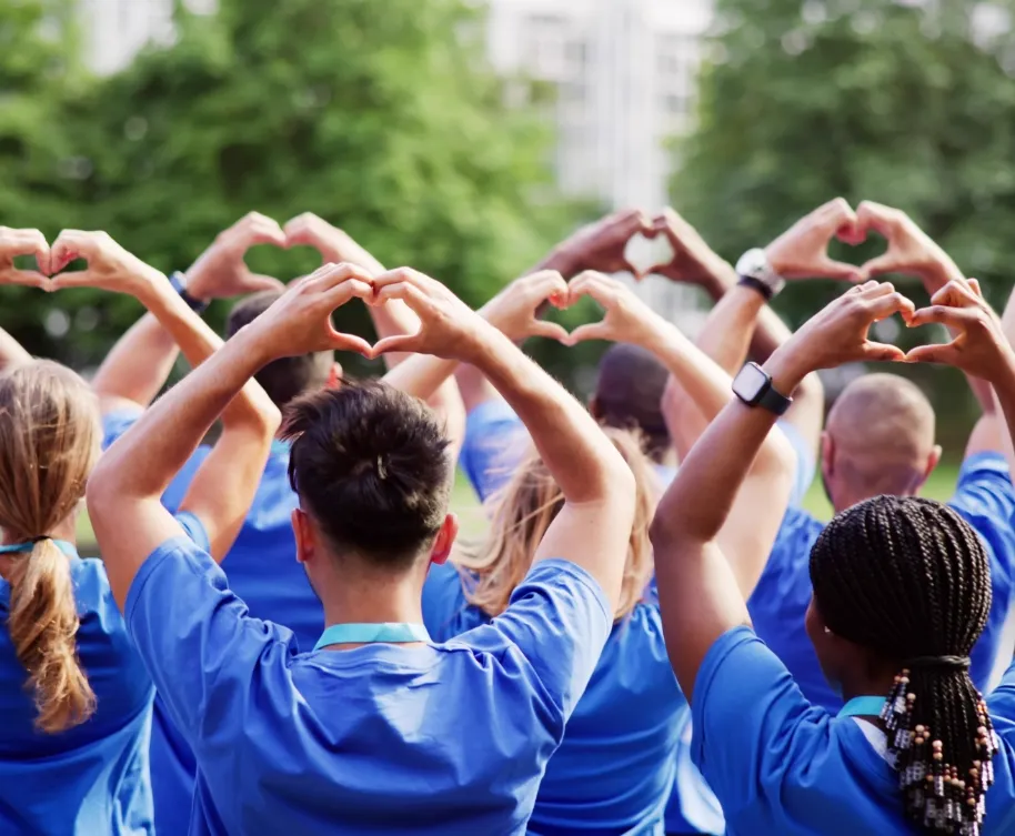 A group of people in blue shirts forming heart shapes with their hands outdoors, promoting unity and love.