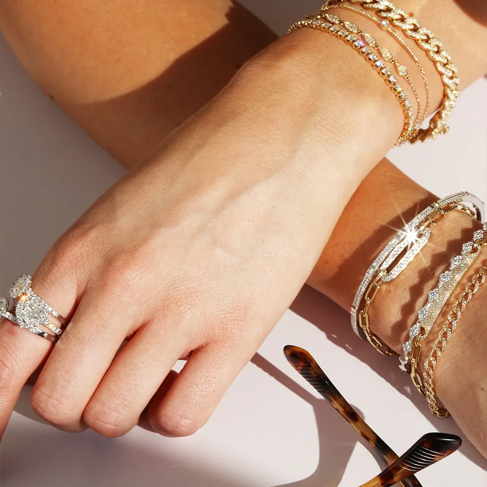 Close-up of a hand adorned with multiple gold and silver bracelets with dazzling diamonds and a sparkling ring.