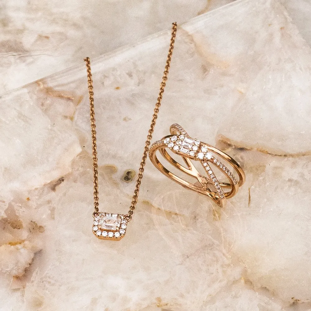 Rose gold necklace and ring set with diamonds on a marble background.
