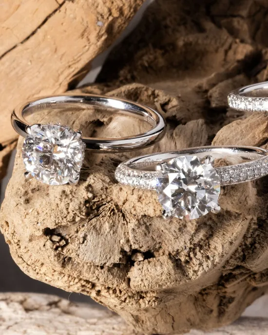 Three elegant solitaire rings with sparkling diamonds displayed on a rustic wooden surface.