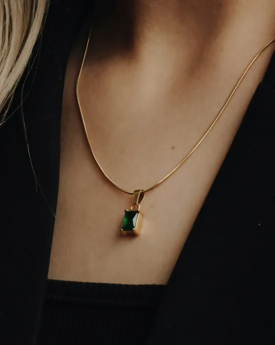 Gold necklace with an emerald pendant worn on a model's neck.