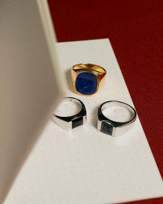 Three rings displayed on a dotted notebook page, featuring a gold lapis lazuli ring and two silver rings.