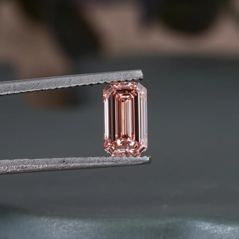 Pink emerald-cut gemstone held by tweezers, showcasing its clarity and brilliance.