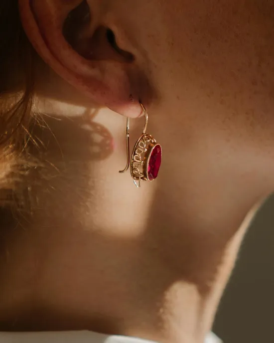 Close-up of a woman's ear wearing a gold earring with a red gemstone.
