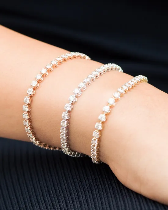 Three elegant tennis bracelets in rose gold and silver on a wrist, showcasing sparkling stones.