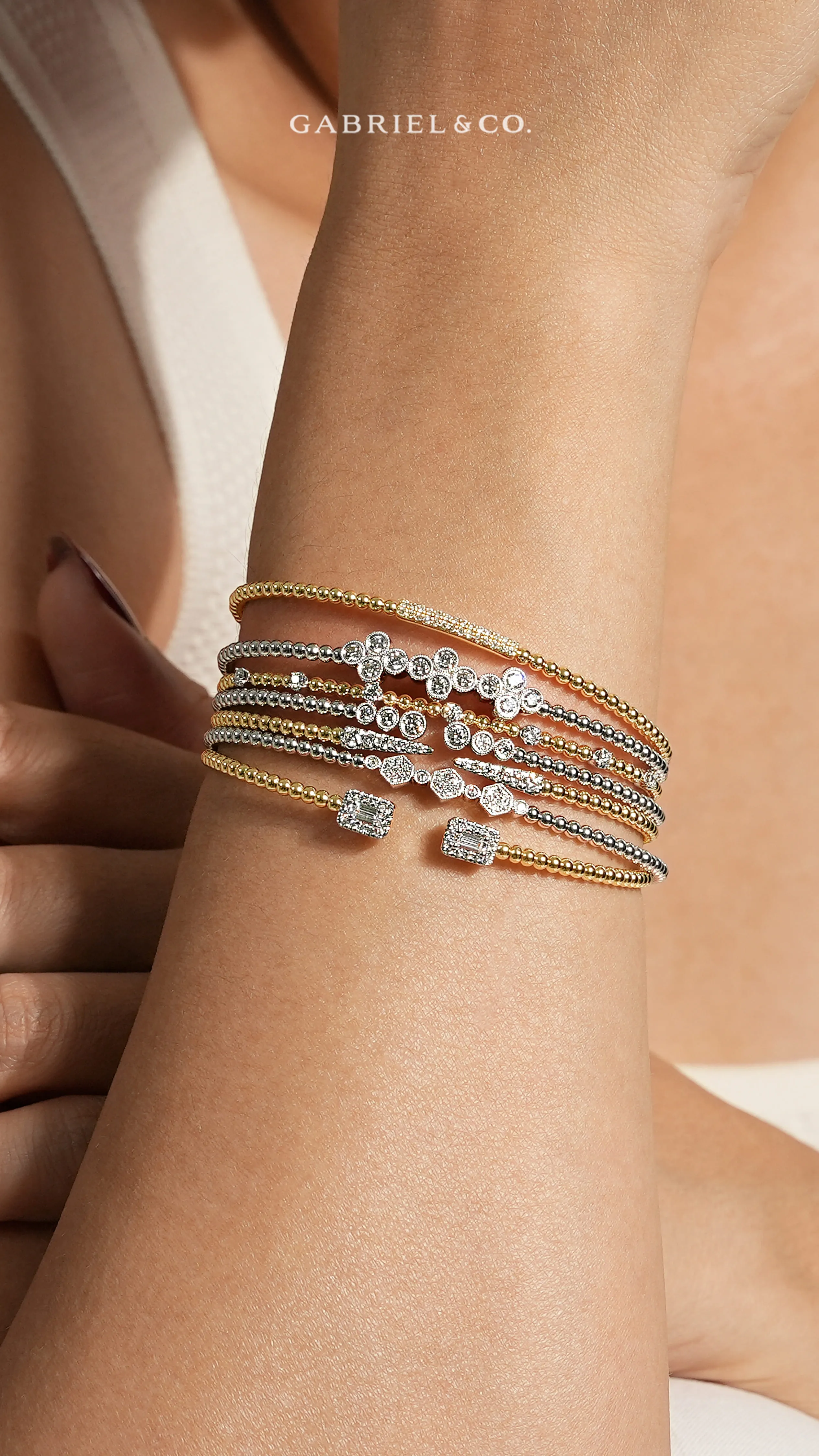 Elegant Gabriel & Co. gold and silver bracelets with diamonds on a wrist. Explore more at Dickinson Jewelers.
