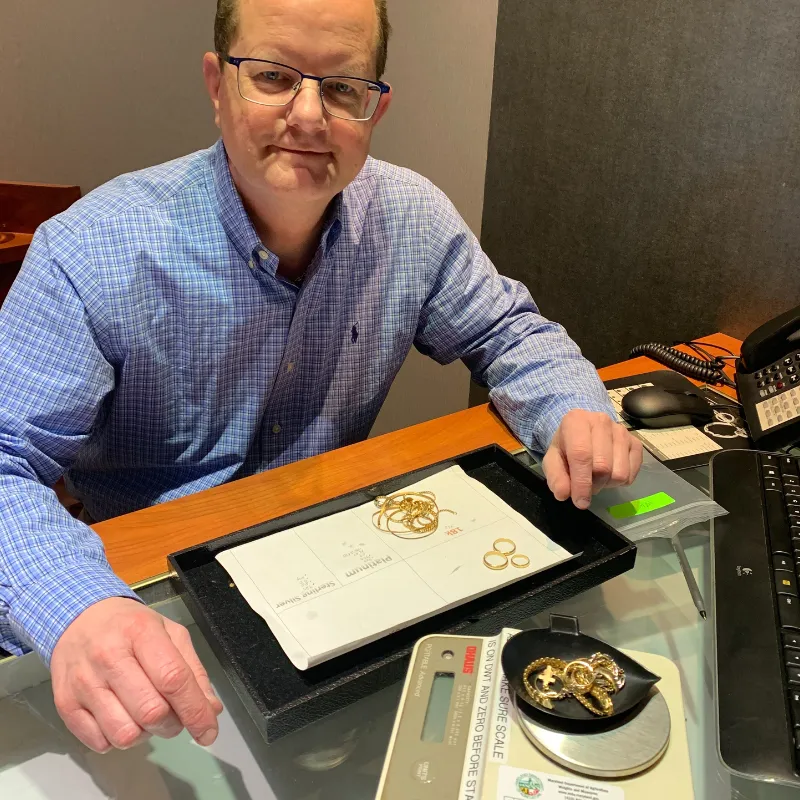 Man in blue shirt evaluating gold jewelry on a desk with a scale.