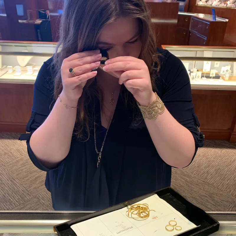 A woman examining jewelry with a loupe in a store.